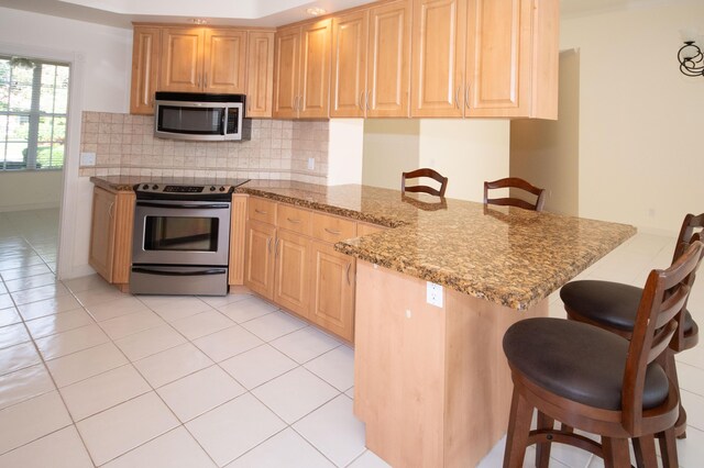 kitchen with stainless steel appliances, a peninsula, a kitchen breakfast bar, decorative backsplash, and light brown cabinetry