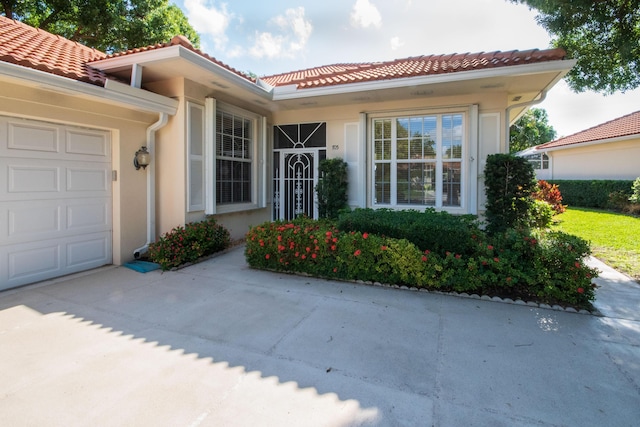 property entrance with an attached garage, a tile roof, stucco siding, and driveway