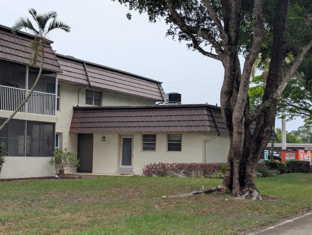view of front facade featuring mansard roof, stucco siding, and a front yard
