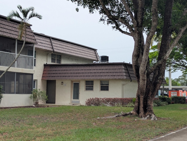 view of front facade featuring mansard roof, stucco siding, and a front yard