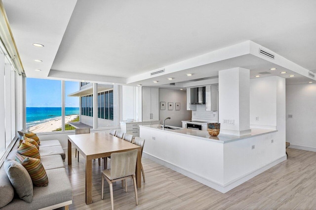 kitchen featuring a sink, wall chimney exhaust hood, recessed lighting, a water view, and a peninsula