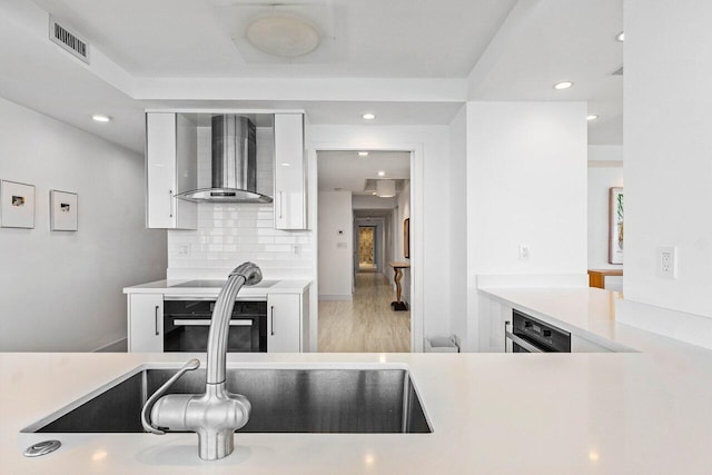 kitchen featuring wall oven, wall chimney range hood, white cabinets, light countertops, and recessed lighting