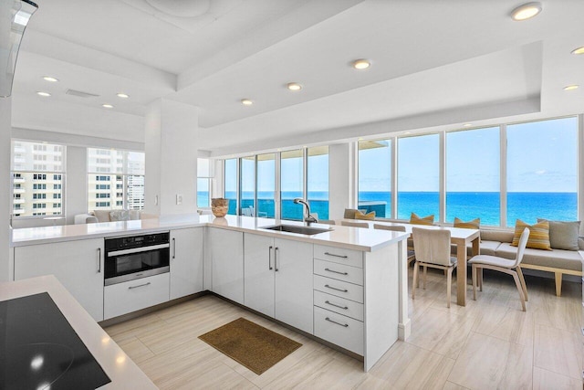 kitchen with a sink, oven, recessed lighting, light countertops, and white cabinets