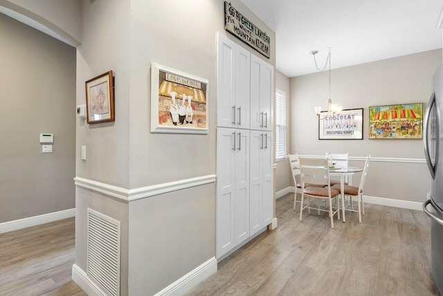 hallway featuring a chandelier, light wood finished floors, and baseboards