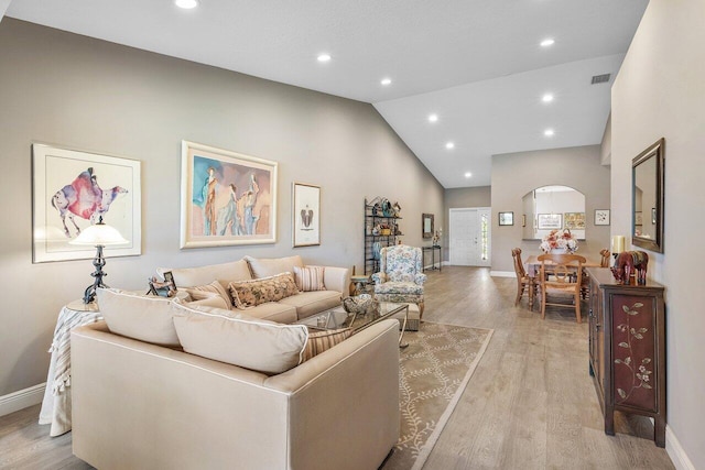 living room featuring arched walkways, baseboards, light wood-style flooring, high vaulted ceiling, and recessed lighting