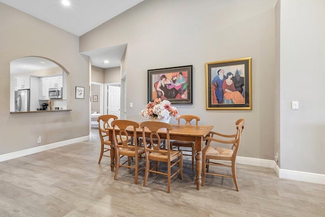 dining area with light wood-style floors, arched walkways, baseboards, high vaulted ceiling, and recessed lighting