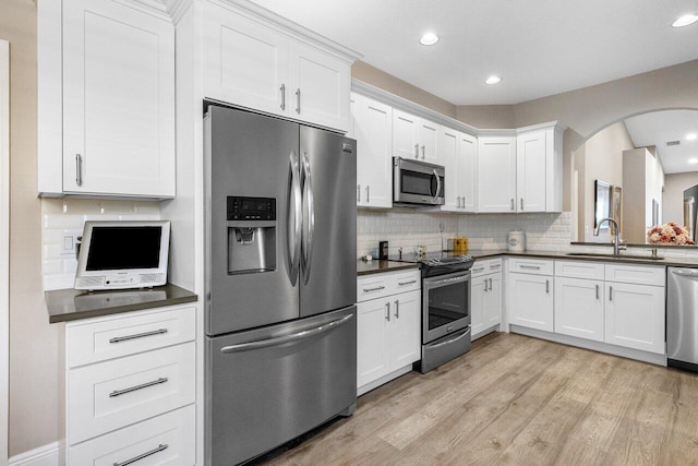 kitchen with stainless steel appliances, a sink, dark countertops, tasteful backsplash, and arched walkways