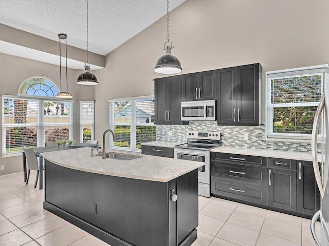 kitchen featuring appliances with stainless steel finishes, a sink, dark cabinets, high vaulted ceiling, and backsplash