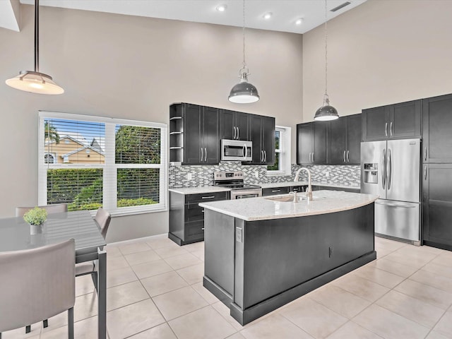 kitchen with stainless steel appliances, a sink, a high ceiling, dark cabinetry, and decorative backsplash