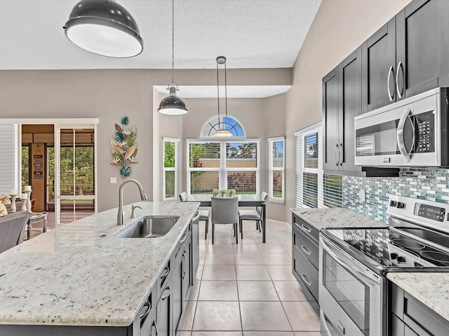 kitchen with appliances with stainless steel finishes, a sink, an island with sink, decorative backsplash, and light stone countertops
