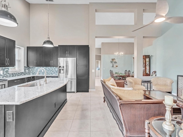 kitchen with a high ceiling, a sink, stainless steel refrigerator with ice dispenser, a chandelier, and light stone counters