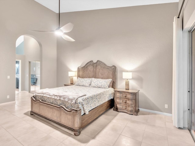 bedroom with arched walkways, light tile patterned flooring, a towering ceiling, baseboards, and a ceiling fan