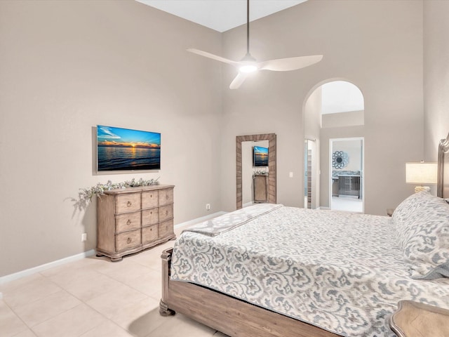 bedroom with a towering ceiling, arched walkways, light tile patterned floors, baseboards, and a ceiling fan