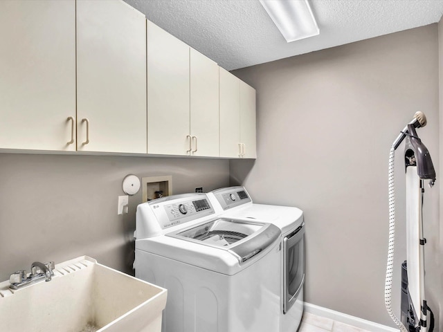 laundry room featuring washer and clothes dryer, cabinet space, a textured ceiling, light tile patterned flooring, and baseboards