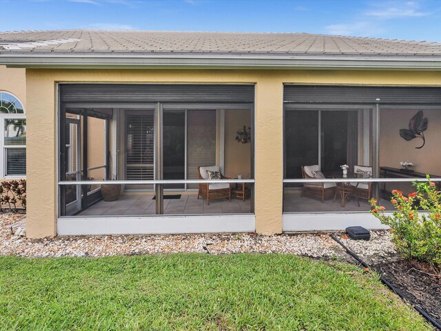 back of property with a sunroom, stucco siding, and a lawn