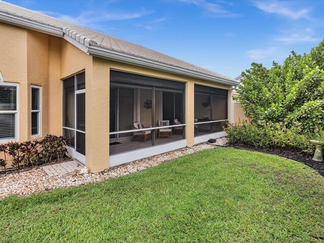 rear view of house featuring a sunroom, a lawn, and stucco siding