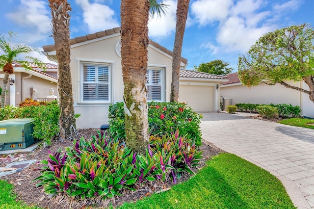 mediterranean / spanish home featuring stucco siding, a tile roof, an attached garage, and decorative driveway