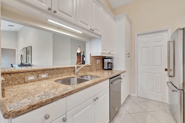 kitchen featuring stainless steel appliances, a sink, white cabinets, light stone counters, and light tile patterned floors