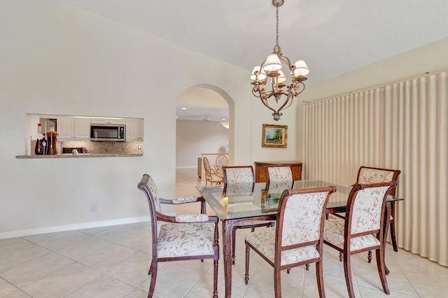 dining area featuring arched walkways, a chandelier, light tile patterned floors, baseboards, and lofted ceiling