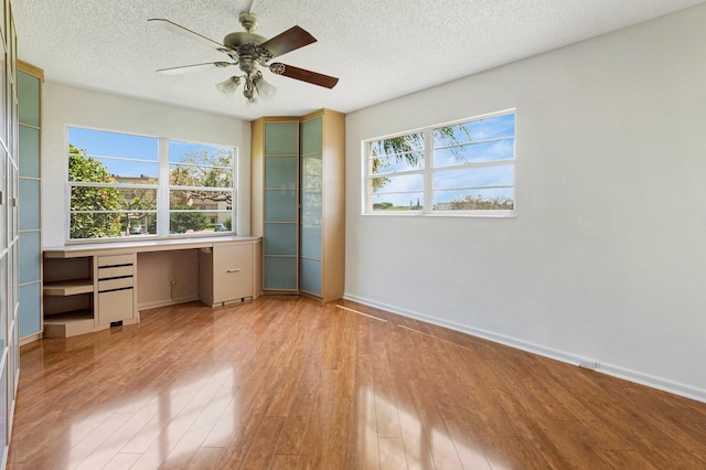 unfurnished office with wood finished floors, a textured ceiling, baseboards, built in study area, and a ceiling fan