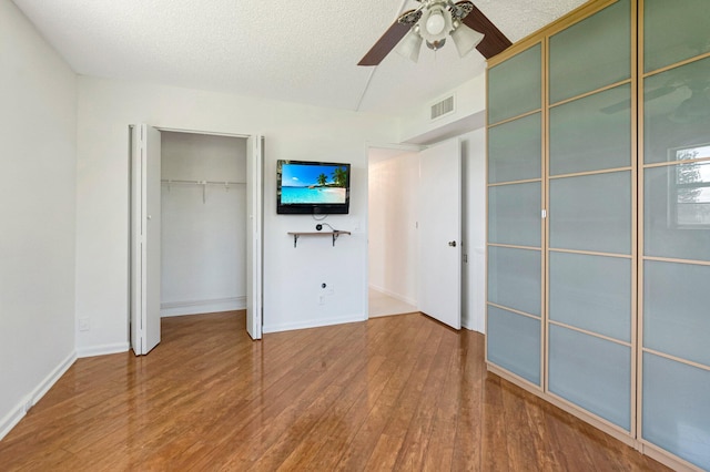 unfurnished bedroom with wood finished floors, ceiling fan, baseboards, a closet, and a textured ceiling