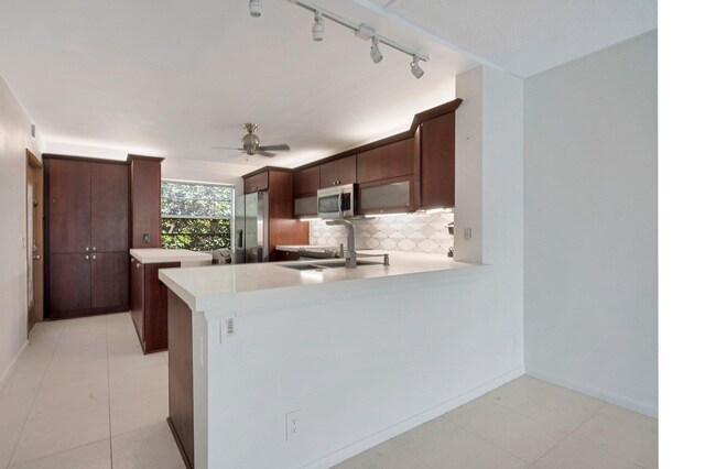 kitchen with appliances with stainless steel finishes, light countertops, backsplash, a peninsula, and rail lighting