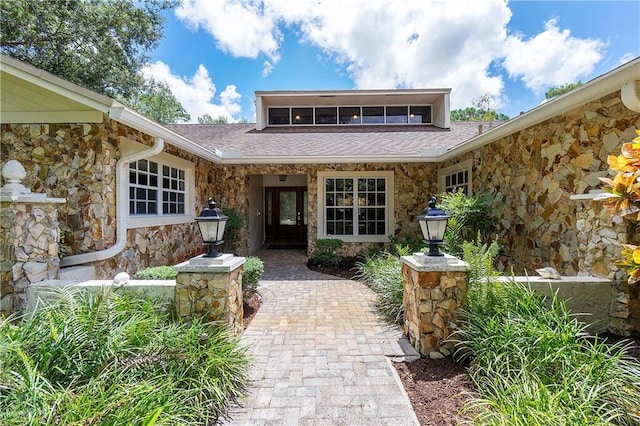 entrance to property featuring stone siding and a shingled roof