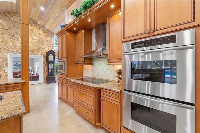 kitchen with wall chimney range hood, lofted ceiling, appliances with stainless steel finishes, tasteful backsplash, and brown cabinets