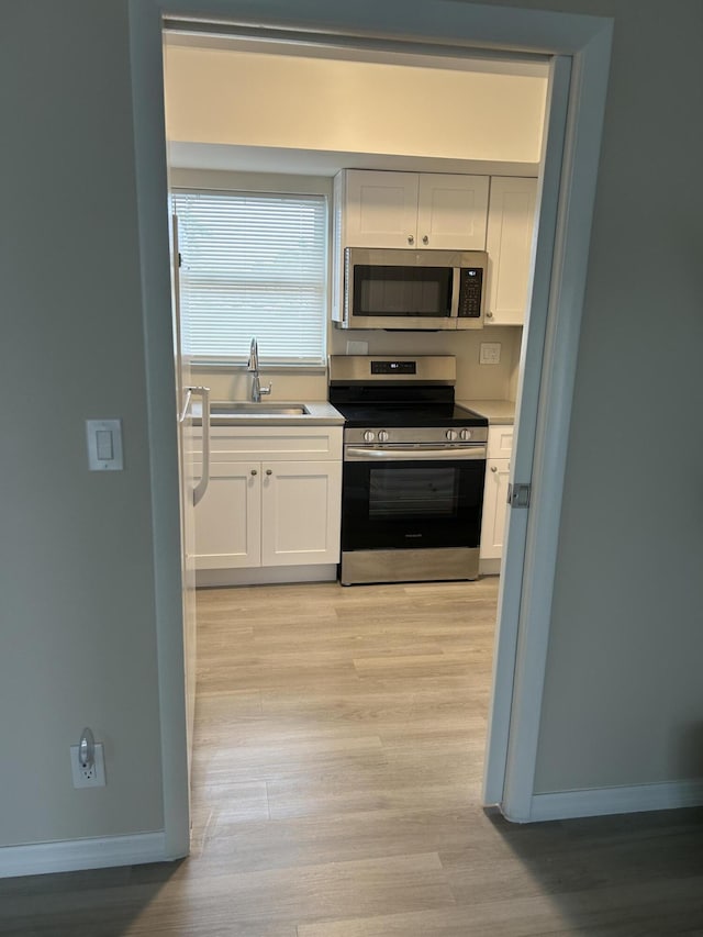 kitchen featuring stainless steel appliances, white cabinetry, a sink, and baseboards
