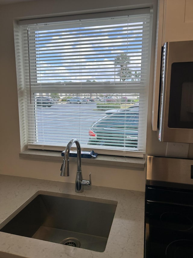 kitchen view of wall oven, stainless steel microwave, a sink, and light stone countertops