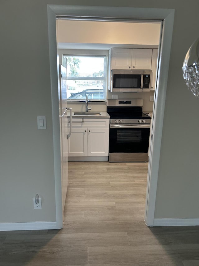 kitchen featuring appliances with stainless steel finishes, a sink, white cabinetry, and baseboards