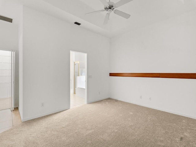 spare room featuring light colored carpet, ceiling fan, baseboards, and a high ceiling
