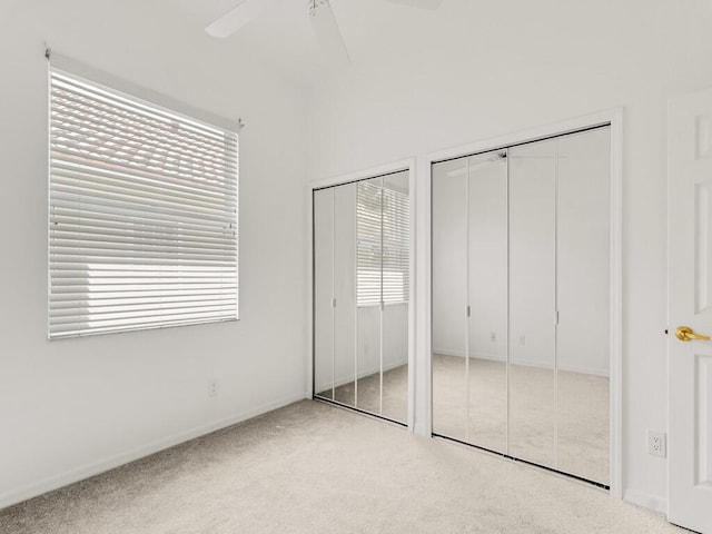 unfurnished bedroom with carpet, two closets, multiple windows, and ceiling fan