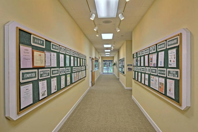 hallway featuring rail lighting, carpet floors, and baseboards