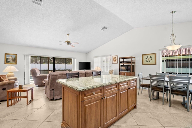 kitchen with brown cabinetry, a ceiling fan, vaulted ceiling, light tile patterned flooring, and light stone countertops
