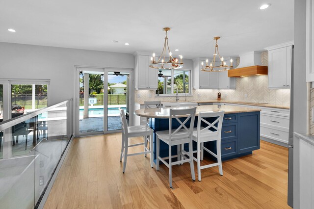 6851 Giralda Cir, Boca Raton, FL 33433 - kitchen featuring light countertops, custom range hood, decorative backsplash, light wood finished floors, and healthy amount of natural light