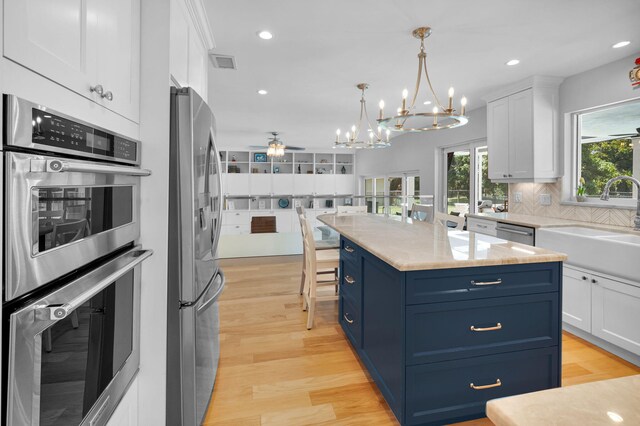 6851 Giralda Cir, Boca Raton, FL 33433 - kitchen with stainless steel appliances, a sink, a chandelier, blue cabinetry, and white cabinetry