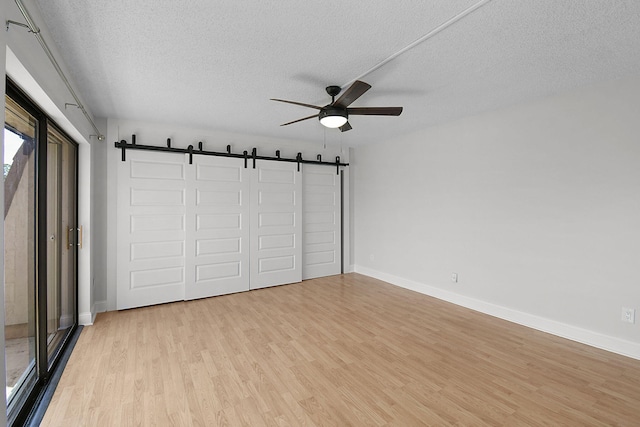 1402 Nebraska Ave Unit 3B, Fort Pierce, FL 34950 - unfurnished bedroom with a barn door, light wood-style floors, a textured ceiling, baseboards, and a ceiling fan