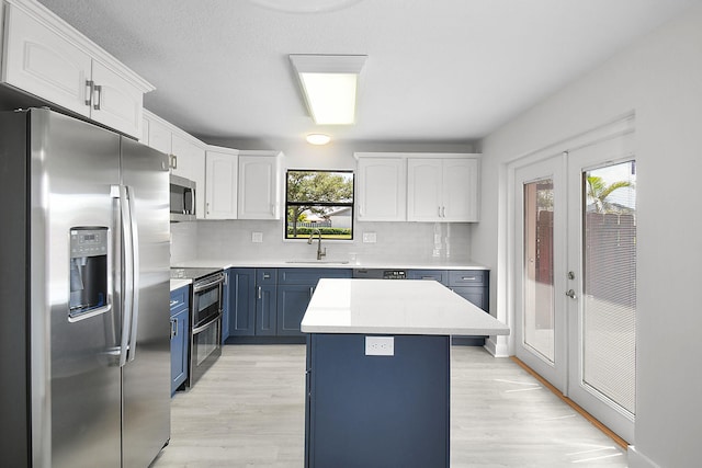1402 Nebraska Ave Unit 3B, Fort Pierce, FL 34950 - kitchen with stainless steel appliances, blue cabinetry, white cabinets, and light wood-style flooring