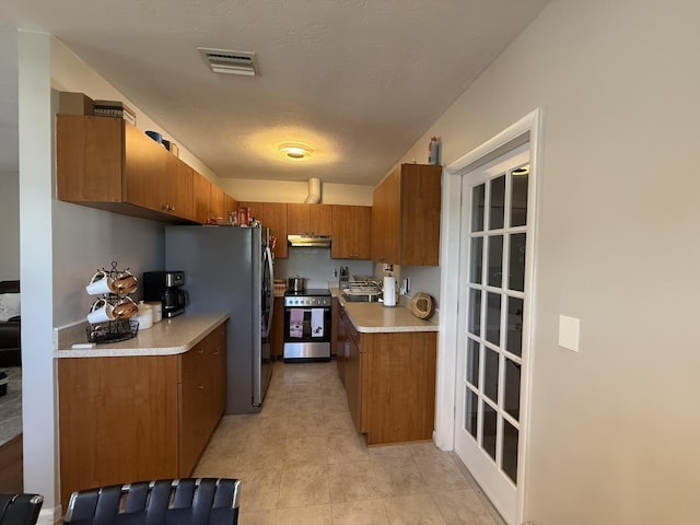 181 Morgans Way, Palm Springs, FL 33461 - kitchen with stainless steel appliances, under cabinet range hood, brown cabinetry, and light countertops