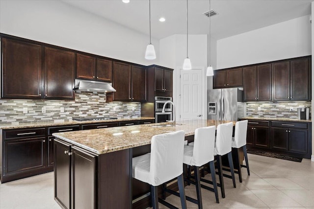 10557 Pisa Rd, Wellington, FL 33414 - kitchen with appliances with stainless steel finishes, under cabinet range hood, light stone countertops, a kitchen bar, and recessed lighting