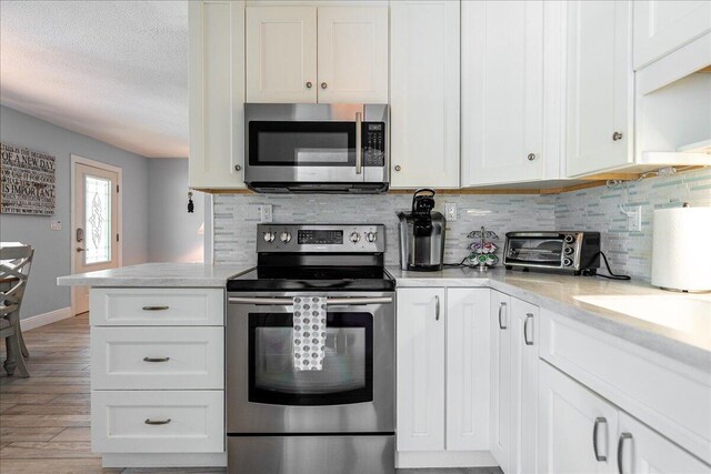71 S Las Olas Dr, Jensen Beach, FL 34957 - kitchen with stainless steel appliances, white cabinetry, tasteful backsplash, light wood-style flooring, and a textured ceiling