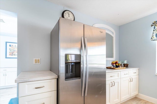 71 S Las Olas Dr, Jensen Beach, FL 34957 - kitchen featuring stainless steel fridge, light wood-type flooring, light countertops, and white cabinetry