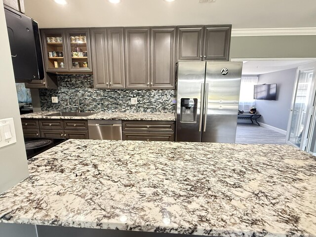 257 SW 5th St, Boca Raton, FL 33432 - kitchen featuring appliances with stainless steel finishes, a sink, light stone counters, glass insert cabinets, and backsplash