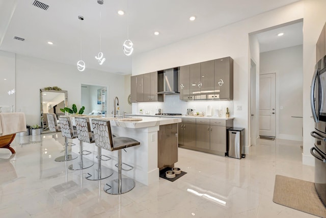 5320 Saint Armands Way, Westlake, FL 33470 - kitchen with wall chimney range hood, gray cabinetry, a breakfast bar area, light countertops, and stainless steel gas cooktop