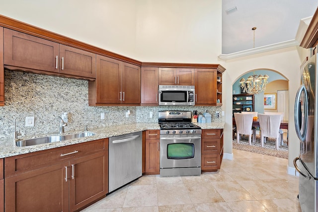 kitchen featuring appliances with stainless steel finishes, a sink, a towering ceiling, a chandelier, and arched walkways