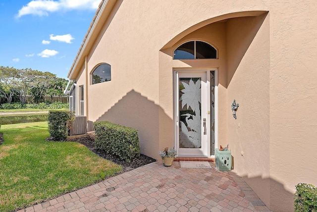 property entrance with a yard, stucco siding, and central AC