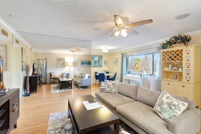 living area with a ceiling fan, ornamental molding, light wood finished floors, and a textured ceiling