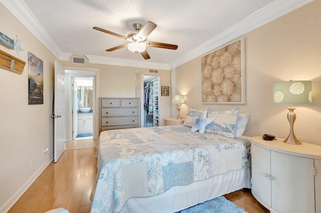 bedroom featuring ornamental molding, light wood-type flooring, a textured ceiling, a spacious closet, and ceiling fan