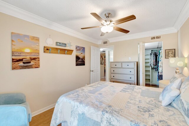 bedroom featuring crown molding, wood finished floors, baseboards, a ceiling fan, and a walk in closet